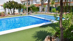 A rectangular swimming pool with a metal railing, surrounded by artificial grass, rocks, and palm trees. - Ola Azul Bungalow V (Benidorm)