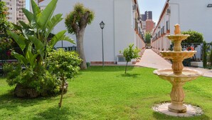 A courtyard with a fountain, a pathway, and a building with a white facade. - Ola Azul Bungalow V (Benidorm)