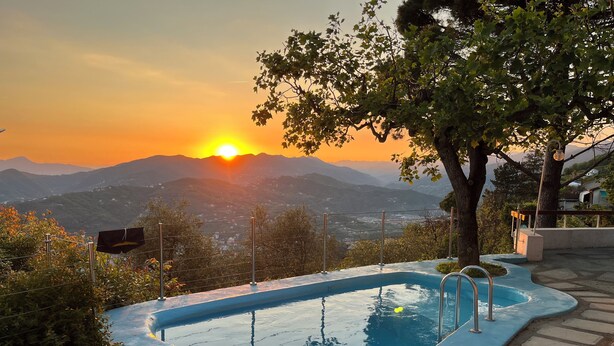 A swimming pool with a view of mountains and a sunset.