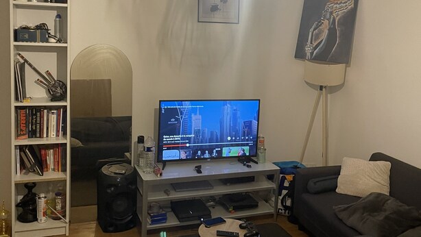 Una sala de estar con televisor, estantería y un cuadro en la pared.