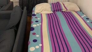 Un dormitorio con una cama, una ventana con cortinas, un radiador y un sofá.