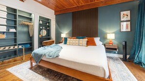 A bedroom with a wooden ceiling, a bed with a blue blanket, a nightstand with a lamp, a wardrobe, and a mirror. - Lincoln Park 3BR Townhome • Rooftop • King Suite • Sleeps 10 (Chicago)