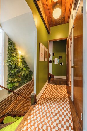 A hallway with a checkered floor, a wooden staircase, a green wall with a plant wall, and a door with a mirror. - Lincoln Park 3BR Townhome • Rooftop • King Suite • Sleeps 10 (Chicago)