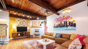 A living room with a television, sofa, coffee table, and a mural of Chicago skyline. - Lincoln Park 3BR Townhome • Rooftop • King Suite • Sleeps 10 (Chicago)