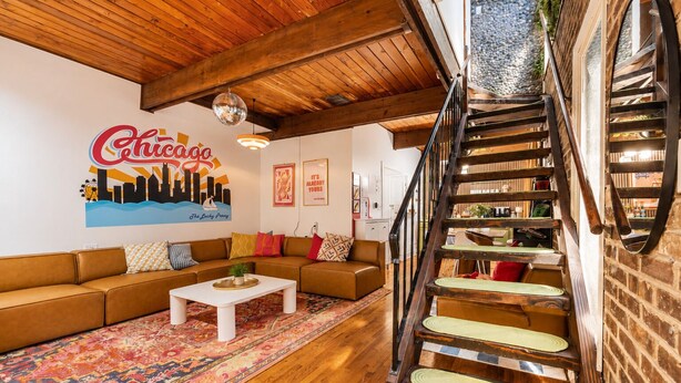 A living room with a brown sofa, a white coffee table, a colorful rug, a wooden staircase, and a wall with a cityscape mural. - Lincoln Park 3BR Townhome • Rooftop • King Suite • Sleeps 10 (Chicago)
