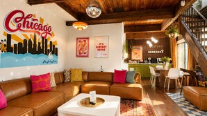 A cozy living room with a brown leather sofa, a white coffee table, and a cityscape mural on the wall. - Lincoln Park 3BR Townhome • Rooftop • King Suite • Sleeps 10 (Chicago)