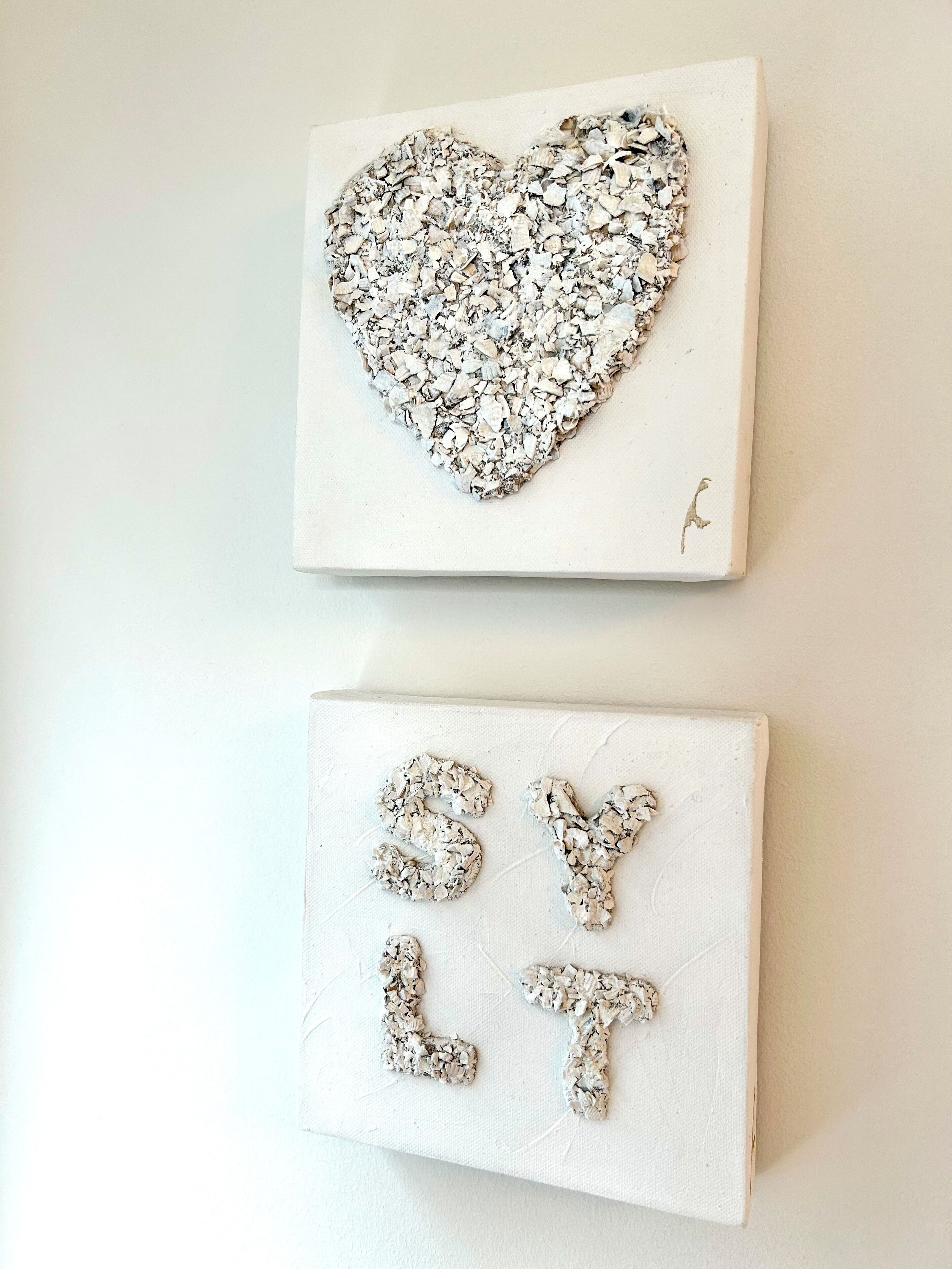 Two white canvases with textured heart and letter designs.