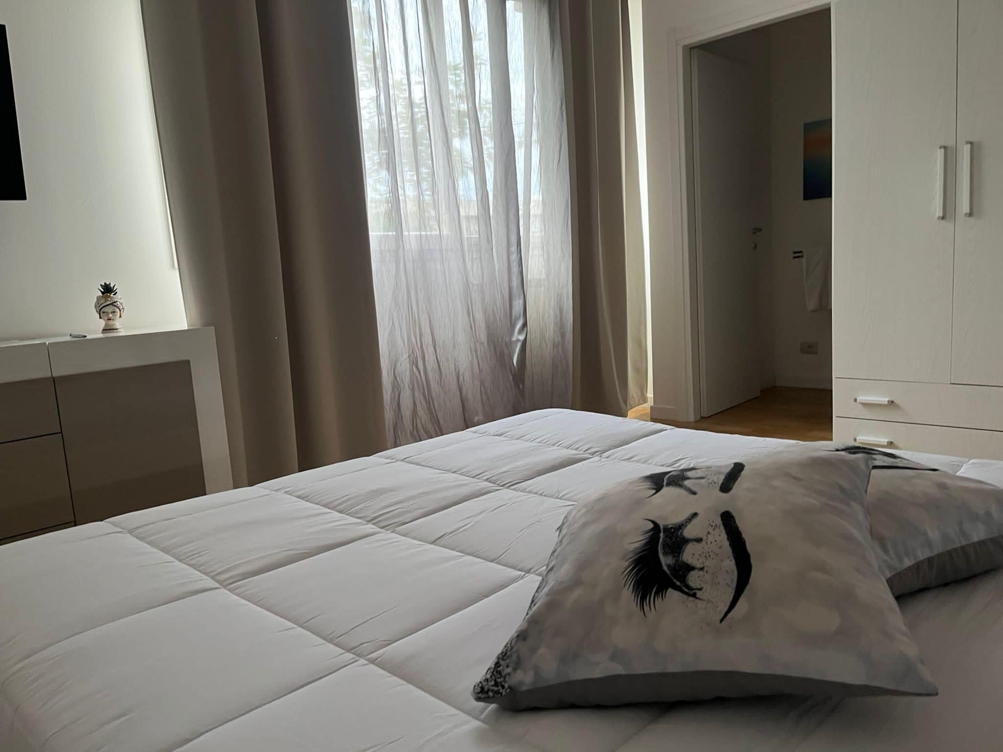 Ein Schlafzimmer mit Bett, Nachttisch, Kleiderschrank und einem Fenster mit Vorhängen.