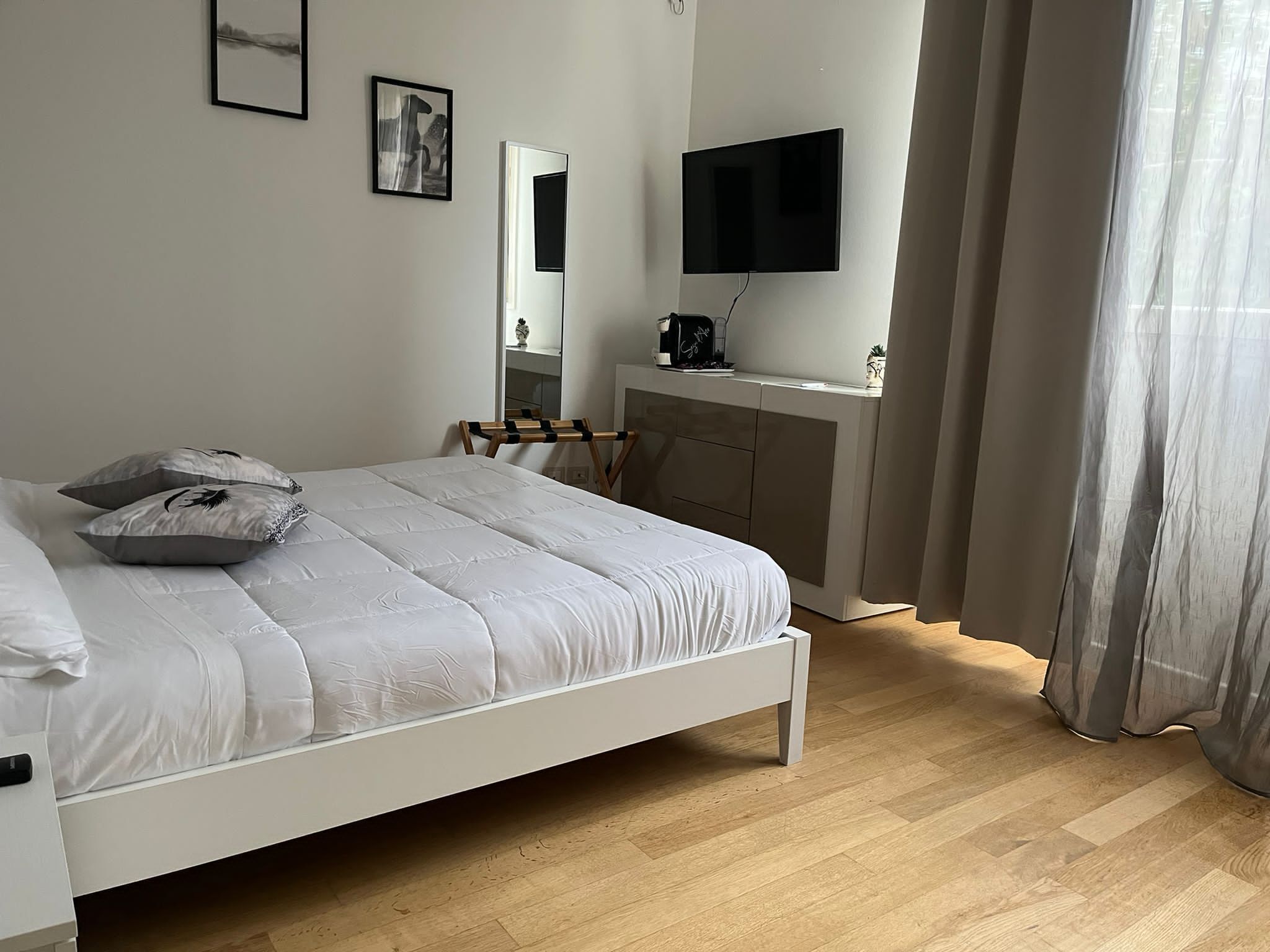 Een slaapkamer met een bed, een dressoir, een televisie en een raam met gordijnen.