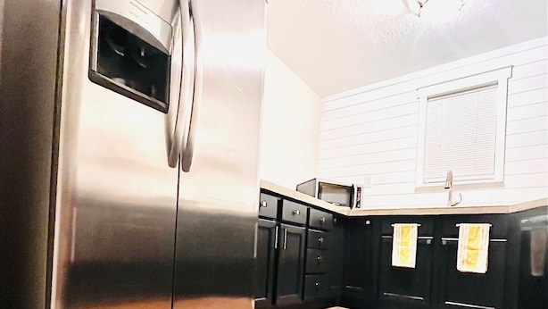 A kitchen with a stainless steel refrigerator, black cabinets, a wooden countertop, and a microwave on the counter.