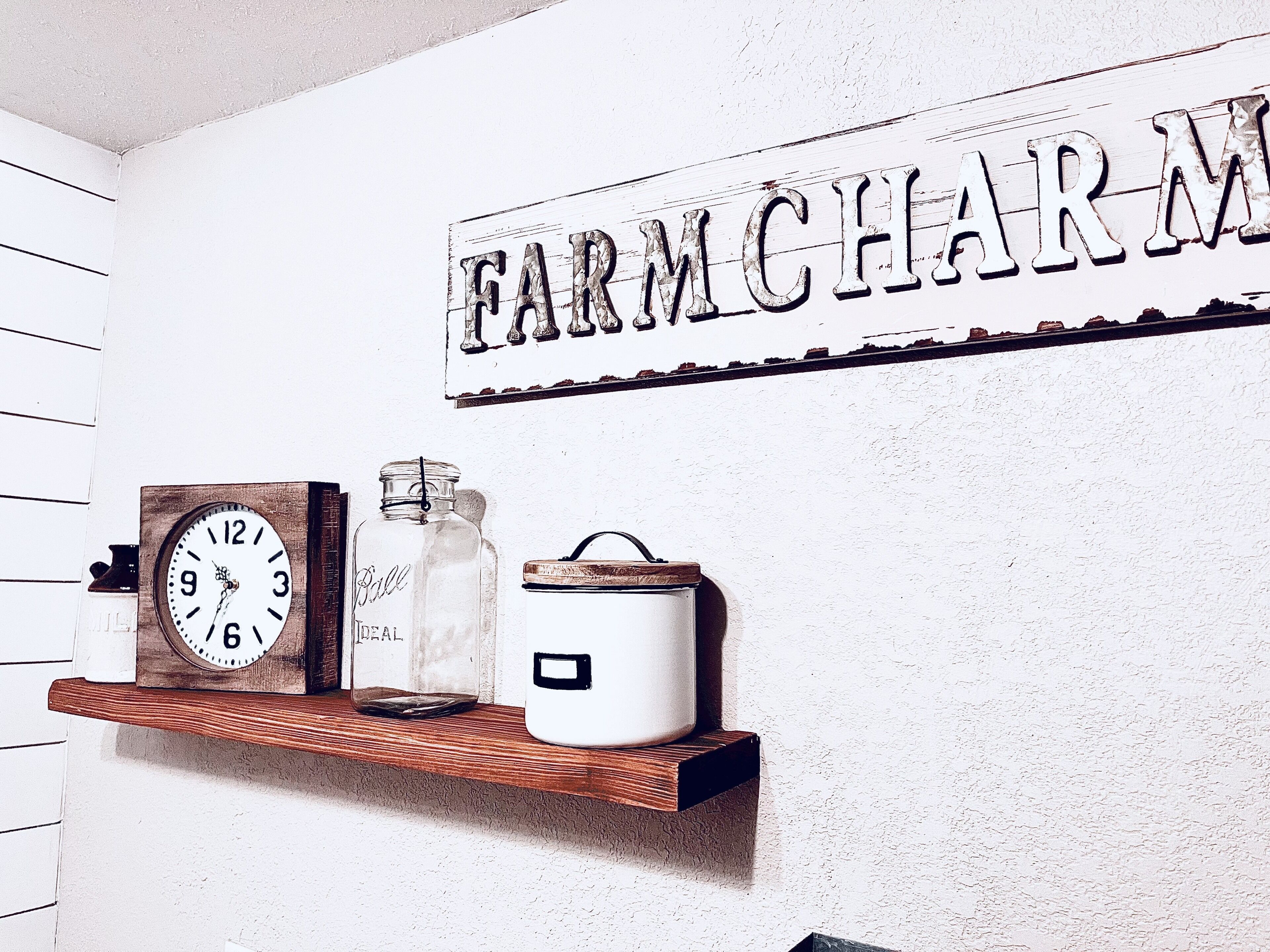 A rustic interior with a shelf displaying a clock, a jar, and a container.