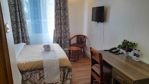 A bedroom with a bed, a desk, a chair, a TV, and a window with curtains.