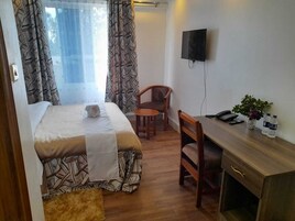 A bedroom with a bed, a desk, a chair, a TV, and a window with curtains.