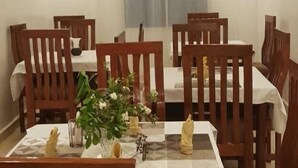 A dining area with wooden chairs and tables, a potted plant, and a window with curtains.