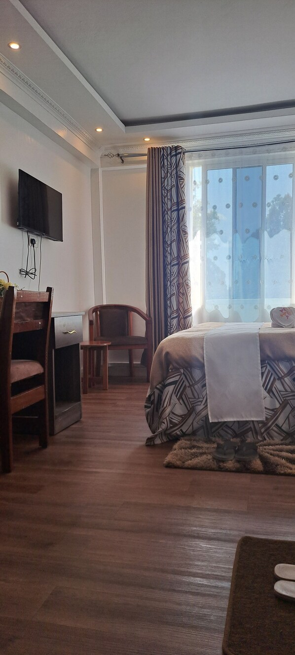 A hotel room with a bed, a desk with a chair, a television, and a window with curtains.