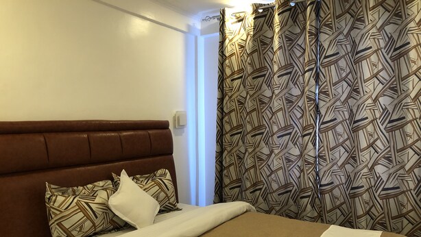 A hotel room with a brown headboard, patterned curtains, and a neatly made bed with a white towel.