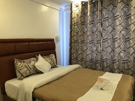 A hotel room with a brown headboard, patterned curtains, and a neatly made bed with a white towel.