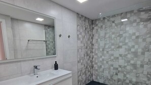 Un baño moderno con un tocador blanco, un espejo grande y una zona de ducha con diseño de baldosas geométricas.