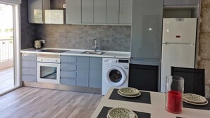 Una cocina moderna con armarios grises, lavadora integrada, refrigerador y un comedor con mesa y platos.