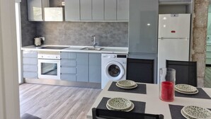 Una cocina moderna con armarios grises, lavadora integrada y un comedor con mesa para dos.