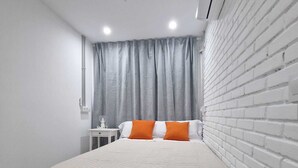 Un dormitorio con cama, mesita de noche, lámpara, ventilador de techo y pared de ladrillo.