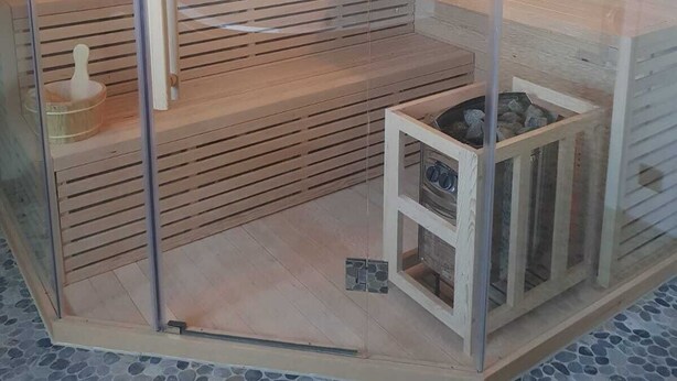 A sauna with a glass door, wooden steps, and a tiled floor.