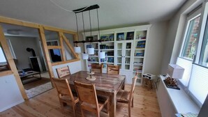 A dining area with a wooden table and chairs, a hanging light fixture, and a bookshelf filled with books and decorative items.