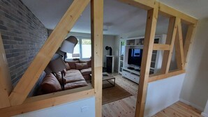 A room with a sloped ceiling, a brown leather sofa, a TV stand, and a lamp.