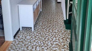 A hallway with a tiled floor, a white console table with a lantern, and a green door.