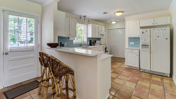 A kitchen with white cabinets, a white refrigerator, and a tiled floor. There is a window with blinds and a door with a doormat. - Pools Paradise: 4  BR, 2  BA House in Wilmington, Sleeps 8 (Wilmington)
