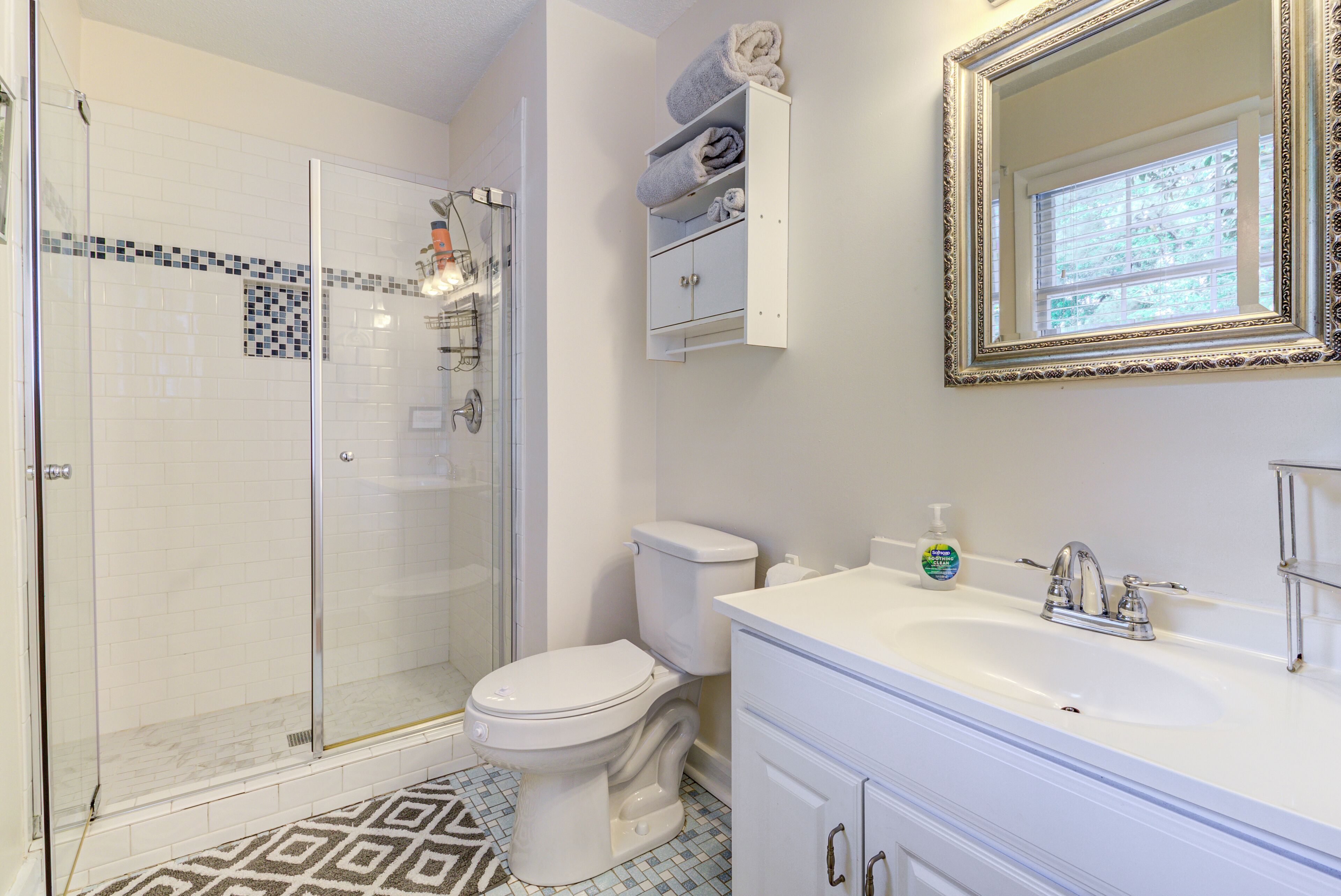A bathroom with a glass-enclosed shower, a toilet, a sink with a mirror, and a towel rack.