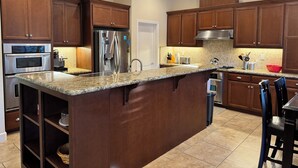 Una cocina moderna con armarios de madera, electrodomésticos de acero inoxidable, encimeras de granito y una isla central.