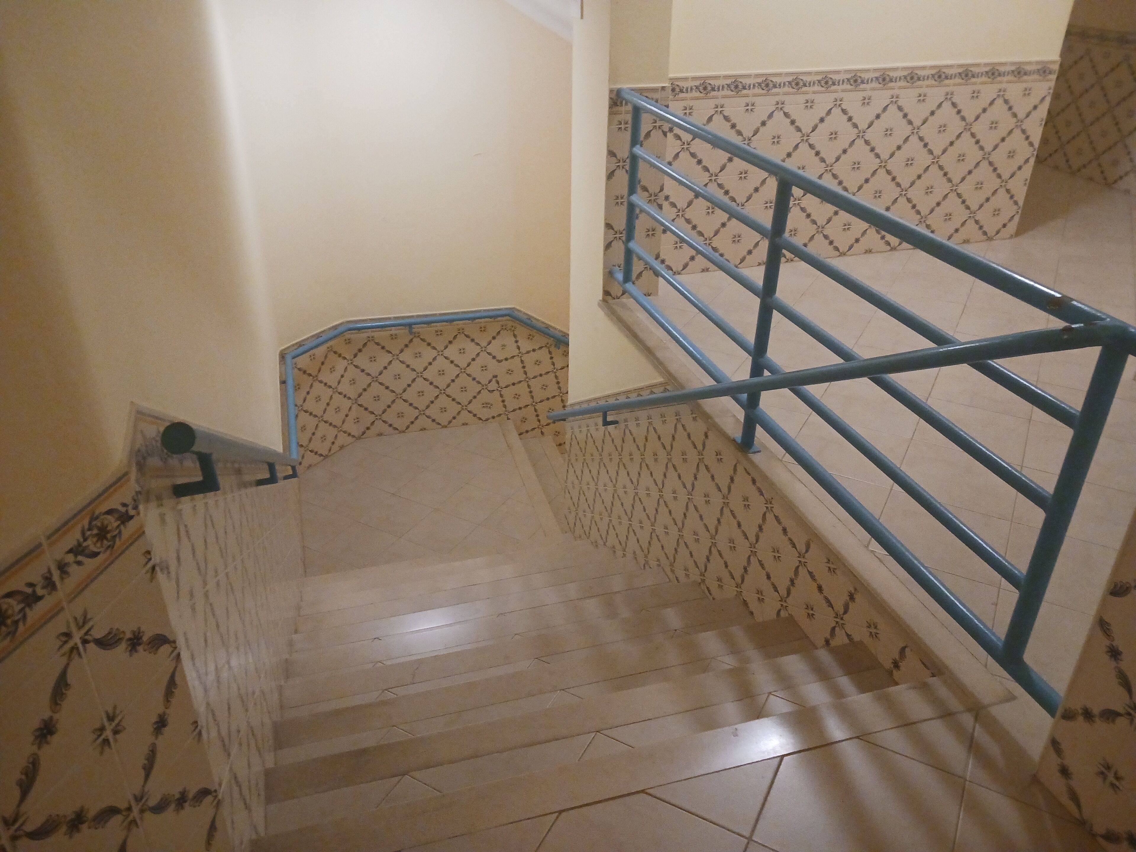 A staircase with a blue handrail and patterned wall tiles.