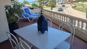 Een balkon met een tafel, stoelen, een bloempot en uitzicht op zee en gebouwen.