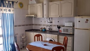 Een keuken met witte kasten, een magnetron, een koelkast en een eettafel met stoelen.