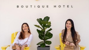 Two women seated on yellow chairs in front of a sign that reads "ALL ARE WELCOME INN BOUTIQUE HOTEL". - All Are Welcome Lawas Boutique Hotel (Lawas)