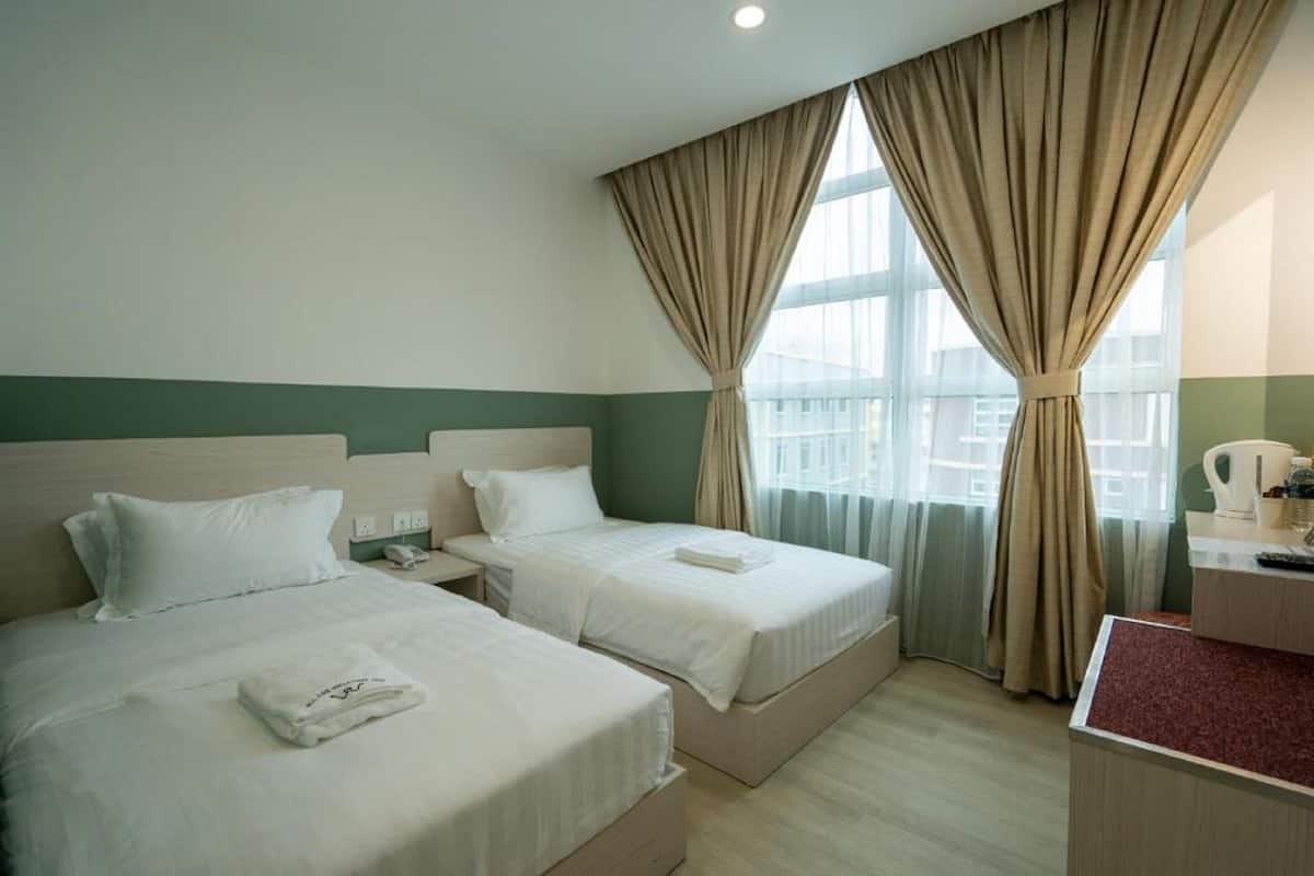 A hotel room with two beds, a desk, and a window with curtains.
