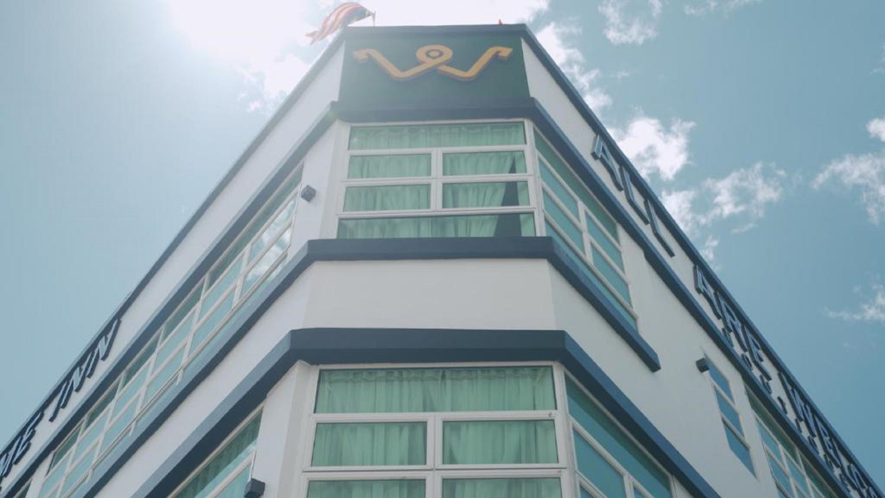 A tall building with a distinctive logo at the top, multiple windows, and a clear sky in the background.