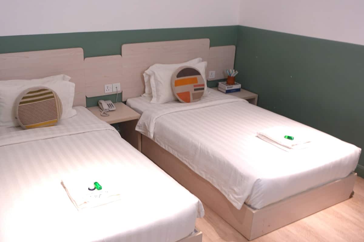 Two single beds with wooden headboards, white bedding, and a small bedside table with a lamp and a phone.
