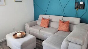 Un soggiorno moderno con un divano componibile, un tavolino in legno con una candela e una parete d'accento blu.