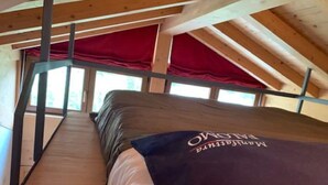 A high-ceilinged room with a wooden floor, a bed with a dark headboard, and a red curtain. - Comfortable alpine-style LA STAFFA hut 5 minutes from Bormio (Valdidentro)