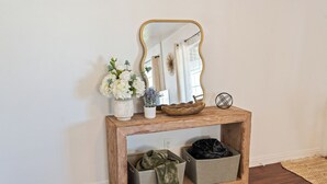 Una consolle in legno con uno specchio, due vasi di fiori e contenitori portaoggetti.