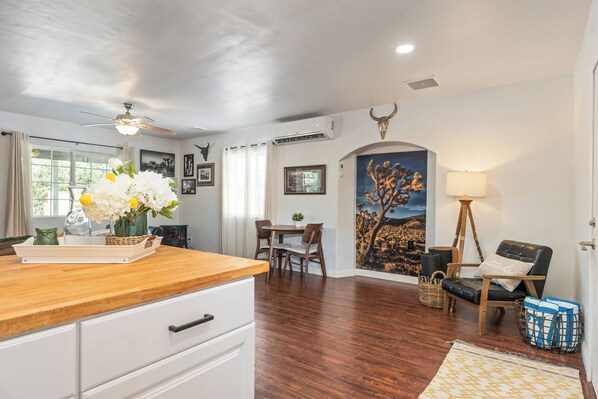 A modern kitchen with wooden countertops, a dining area with a table and chairs, and a living area with a sofa and lamp. - Village House - Hot Tub, Pool, walk to downtown shops (Joshua Tree)