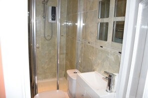 Bathroom features a glass-enclosed shower, handheld showerhead, and wall-mounted faucet.