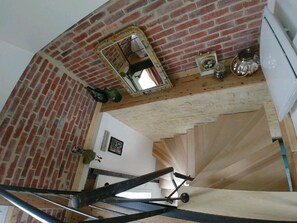 Un escalier avec un mur en briques et un plancher en bois. Un miroir est accroché au mur, et un cadre photo se trouve en dessous.
