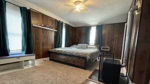 Ein Schlafzimmer mit Bett, einem Fenster mit Vorhängen, einem Deckenventilator und einer Heizung.