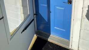 Eine blaue Tür mit Zahlenschloss, einem kleinen Fenster und einer Fußmatte.