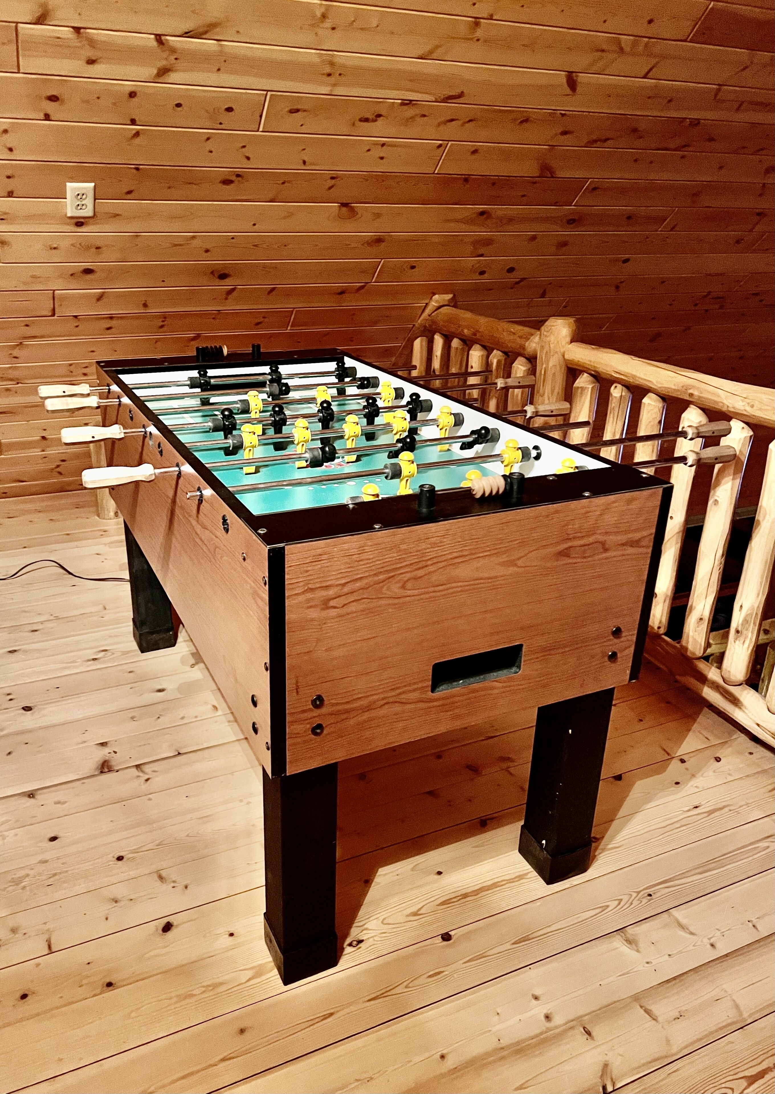 A wooden foosball table in a room with wooden flooring and walls.