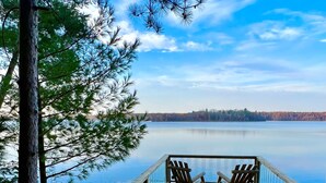 A wooden deck with chairs facing a calm lake, surrounded by trees.