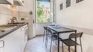 A compact kitchen with a gas stove, a kettle, and a window overlooking a building. There is a dining area with a table and chairs. - Few steps from Vatican City - 2 double rooms (Roma)